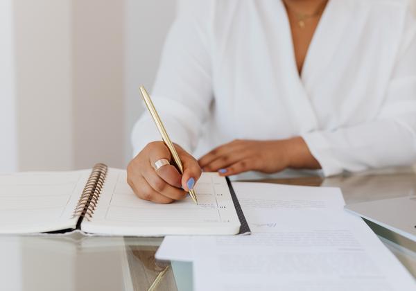 Woman writing in a notebook with documents on a table